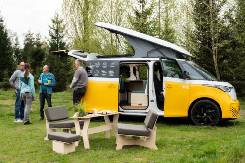 Drie mensen staan buiten bij een geel camperbusje