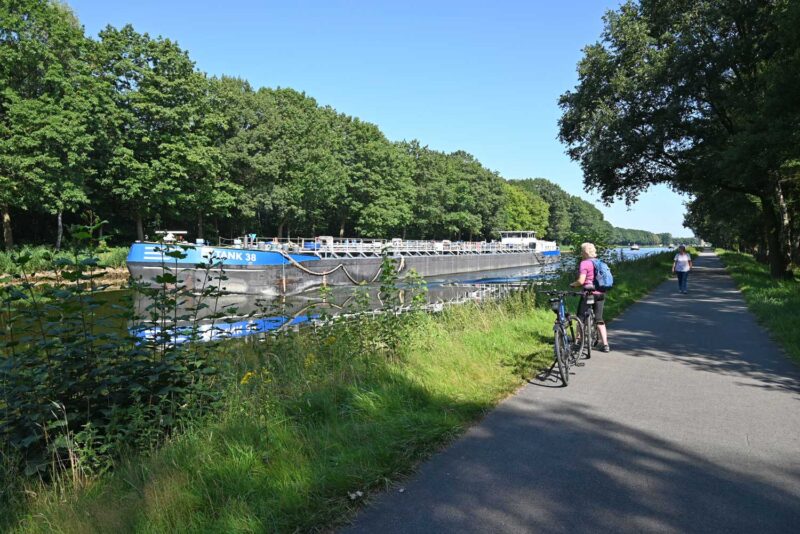 Fietsen langs de Ems met op de achtergrond een groot vrachtschip dat vaart op het kanaal